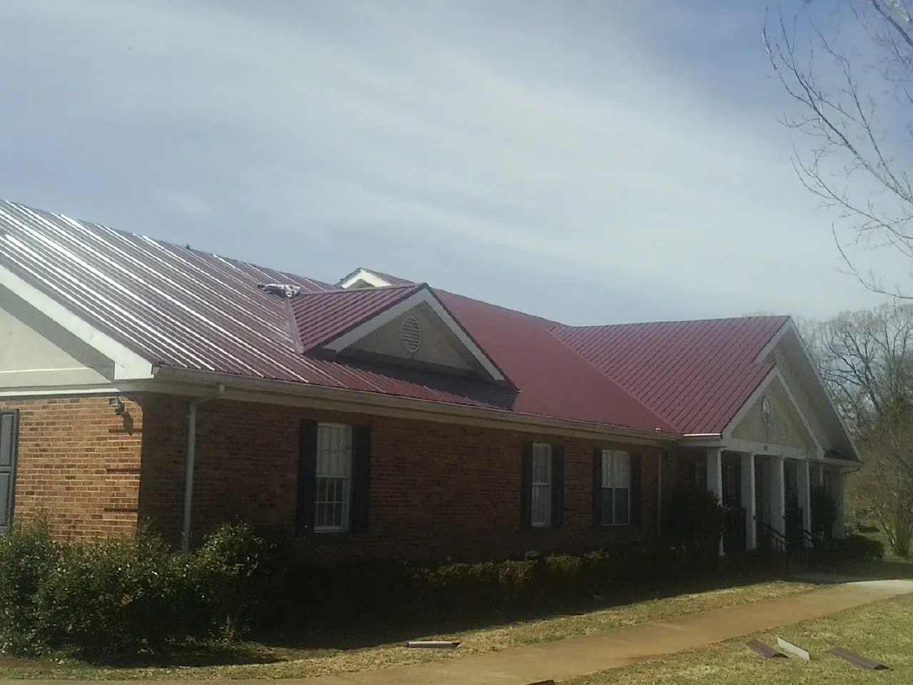 Red metal roof with gabled entries on a long brick building, from a Hail Damage Roof Repair job in Abbeville