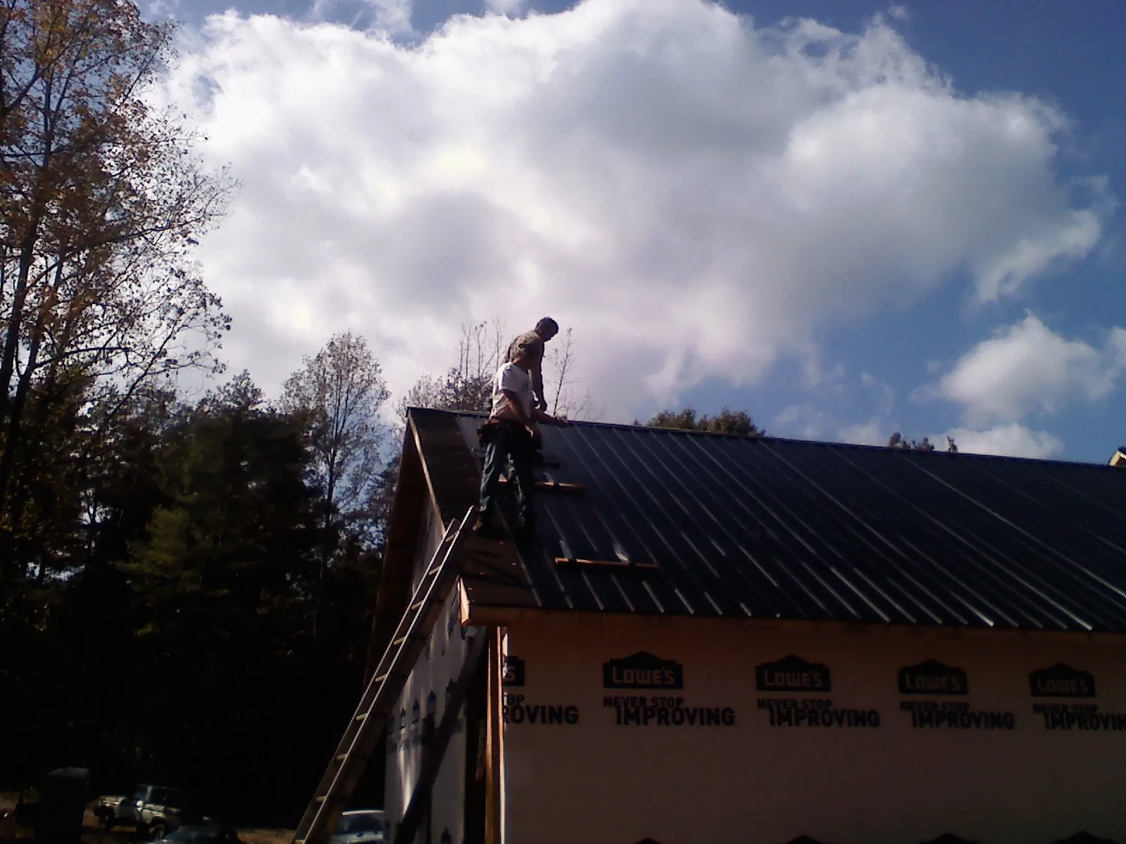 Roofer fastening dark metal panels high against a cloudy sky, from a Roof Inspection job in Abbeville